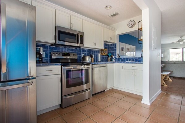 Equipped with stainless steel appliances, this kitchen offers a clean and contemporary space with white cabinetry and a blue-tiled backsplash.