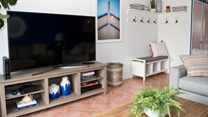 Ein Wohnzimmer mit Flachbildfernseher, Bücherregal, einem kleinen Tisch, einer Couch und einer Topfpflanze.