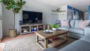 Ein Wohnzimmer mit Fernseher, Sofa, Couchtisch und einer Pflanze.