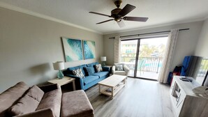 Ein modernes Wohnzimmer mit einem blauen Sofa, einem beigen Sofa, einem Holztisch und einem Deckenventilator.