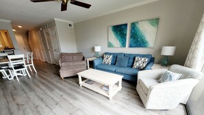 Ein modernes Wohnzimmer mit einem blauen Sofa, weißen Sessel, einem Couchtisch und einem Deckenventilator.