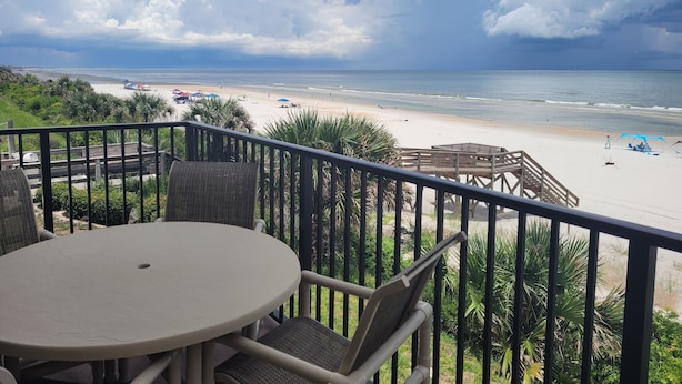 A balcony with a view of a beach, including a wooden deck and wicker furniture. - Oceanfront 2 Bedroom Townhouse.  Summerhouse Unit 353 (ST AUGUSTINE)