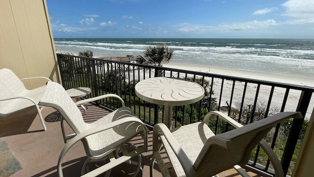 A balcony with a view of the ocean, featuring a table and chairs.
