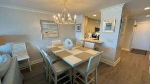 A dining area with a table and chairs, a chandelier, and a kitchen in the background.