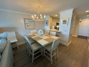 A dining area with a table and chairs, a chandelier, and a kitchen in the background.