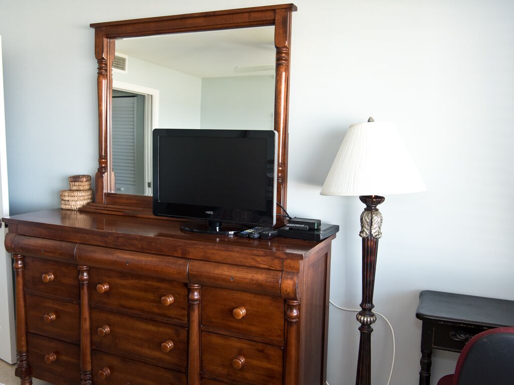 Une commode en bois, un téléviseur à écran plat, une lampe et une petite table.