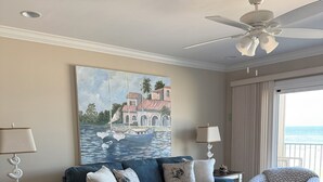 A living room with a blue sofa, a white coffee table, and a patterned armchair. There is a painting of a coastal scene on the wall. - Oceanfront 2 Bedroom Townhouse.  Summerhouse Unit 357 (ST. AUGUSTINE)
