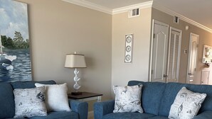 A living room with two blue sofas, a white coffee table, and a painting of boats on the wall. - Oceanfront 2 Bedroom Townhouse.  Summerhouse Unit 357 (ST. AUGUSTINE)