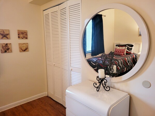 A bedroom with a white closet, a round mirror, and a bed with patterned bedding.