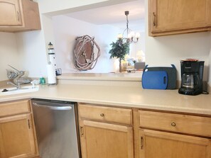 Una cocina con armarios de madera, lavavajillas, cafetera y un adorno en la pared.