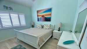 A bedroom with a bed, nightstands, a dresser, a mirror, a painting, and a window with blinds.