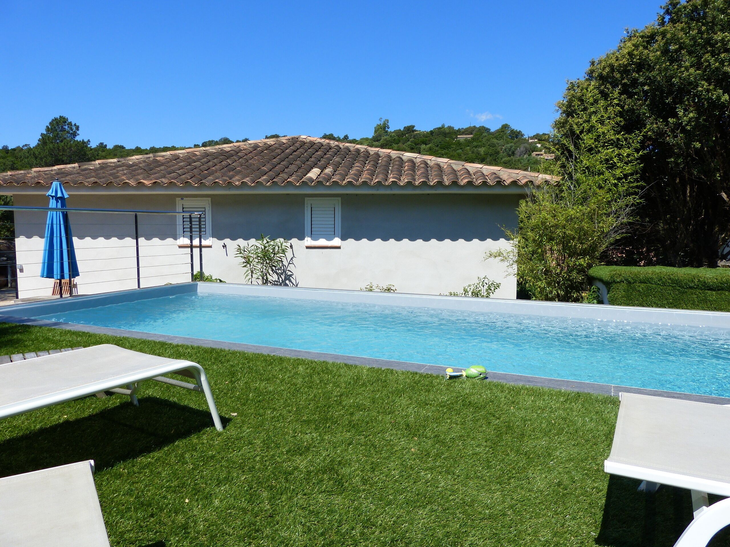 A swimming pool with a tiled roof, surrounded by a well-maintained lawn and a few lounge chairs.