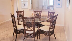 A dining area with a round glass table surrounded by six wicker chairs with cushioned seats. - Ocean view 3 bedroom 2 Bath Flat.  Summerhouse Unit 425 (ST. AUGUSTINE)