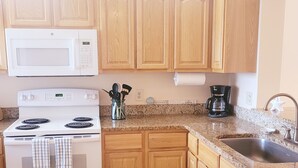 A kitchen with wooden cabinets, a white stove, a microwave, a coffee maker, and a granite countertop. - Ocean view 3 bedroom 2 Bath Flat.  Summerhouse Unit 425 (ST. AUGUSTINE)