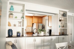 Une cuisine avec des meubles blancs, un plan de travail noir et divers objets décoratifs disposés sur des étagères.