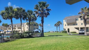A grassy area with palm trees, a pool, and a building with multiple balconies. - Oceanview 2 Bedroom Flat  Summerhouse 446 (ST. AUGUSTINE)