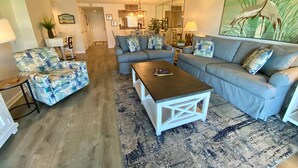 A living room with a sofa, armchair, coffee table, and a large painting of a bird. - Oceanview 2 Bedroom Flat  Summerhouse 446 (ST. AUGUSTINE)