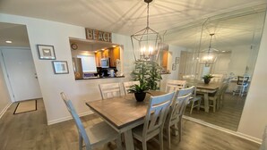 A dining area with a wooden table and chairs, a potted plant, and a kitchen in the background. - Oceanview 2 Bedroom Flat  Summerhouse 446 (ST. AUGUSTINE)