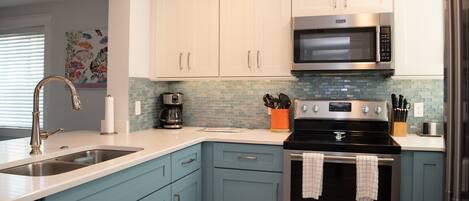 A modern kitchen with light blue cabinets, a stainless steel range, a coffee maker, and a microwave.