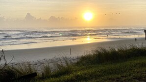 A beach with the sun setting over the ocean, a person walking on the sand, and birds flying in the sky. - Oceanfront 2 Bedroom Flat  Summerhouse Unit  452 (ST. AUGUSTINE)
