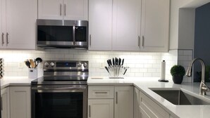 A modern kitchen with stainless steel appliances, white cabinetry, and a built-in sink. - Oceanfront 2 Bedroom Flat  Summerhouse Unit  452 (ST. AUGUSTINE)