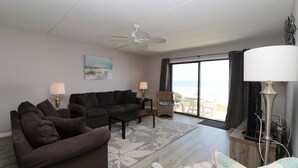 Ein Wohnzimmer mit einer Sofagarnitur, einem Couchtisch, einer Stehlampe und Blick auf den Ozean durch ein großes Fenster.