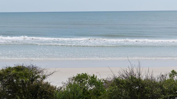 Ein Strand mit sanften Wellen und blauem Himmel.