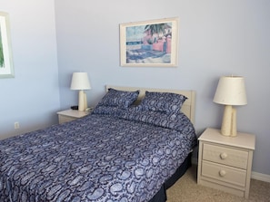 A bedroom with a bed, two bedside tables, a nightstand, a lamp, and a framed picture on the wall. - Oceanfront 2 Bedroom Townhouse  Summerhouse Unit 456 (ST. AUGUSTINE)
