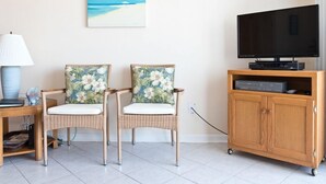 A living room with two wicker chairs, a wooden cabinet with a TV, and a painting of a beach scene. - Oceanfront 2 Bedroom Townhouse  Summerhouse Unit 456 (ST. AUGUSTINE)