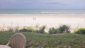 A beach view with a chair in the foreground, a fence, and two people in the distance.