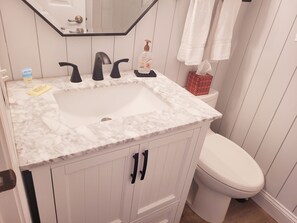A bathroom with a white sink, black faucets, and a white toilet. There is a mirror above the sink and a towel rack with towels.