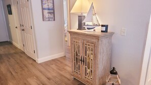 A hallway with wooden flooring, a decorative cabinet with glass doors, a wall-mounted lamp, and a small lantern.