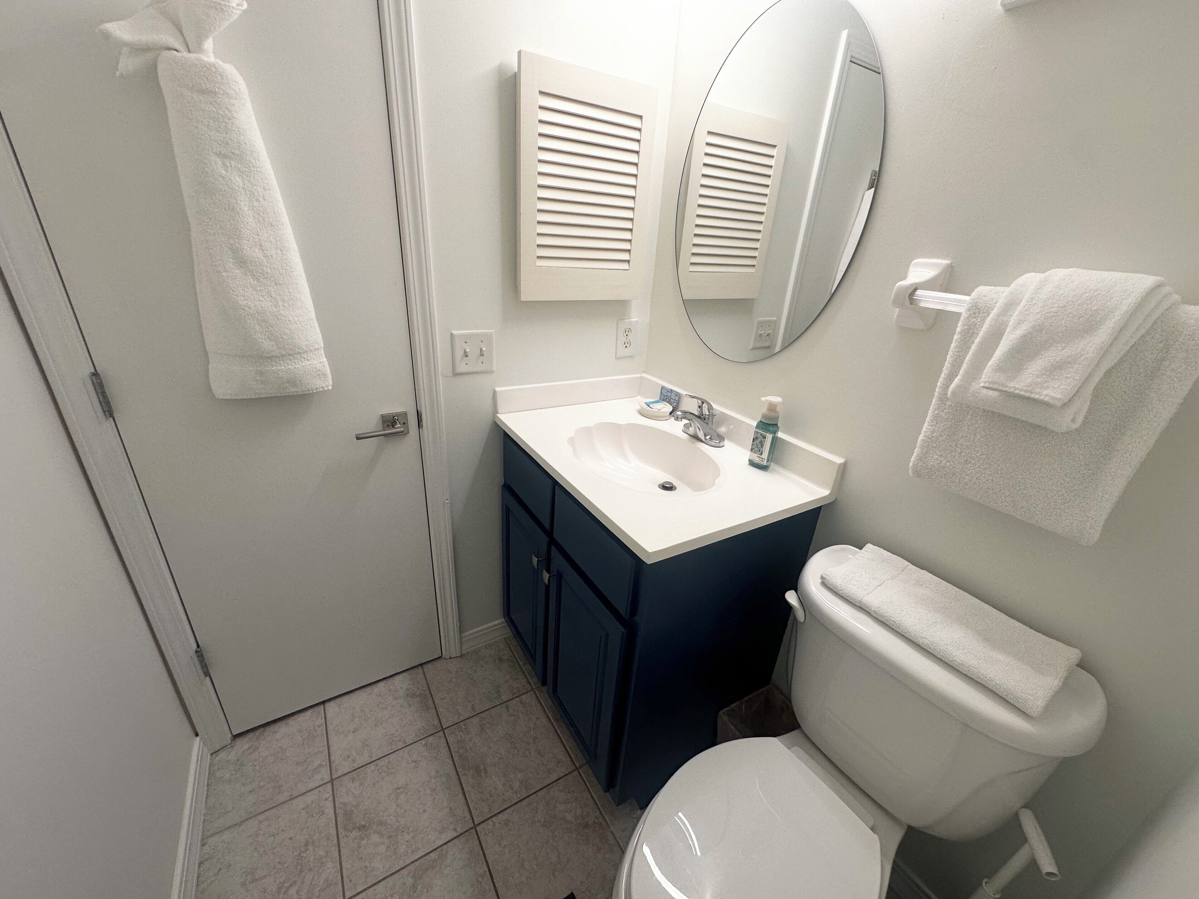 Un baño con un lavamanos blanco, un espejo y un inodoro. Hay toallas colgadas en la pared y una puerta con una toalla.