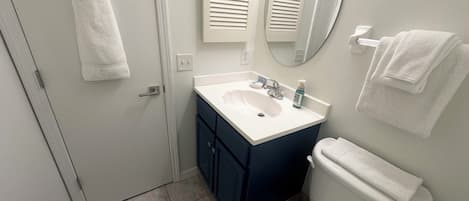 Un baño con un lavamanos blanco, un espejo y un inodoro. Hay toallas colgadas en la pared y una puerta con una toalla.