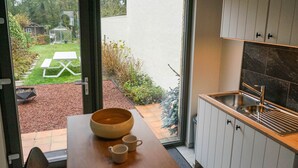 Eine moderne Küche mit einem großen Fenster, einem Holztisch mit Schüssel und Tassen sowie einem Spülbecken.