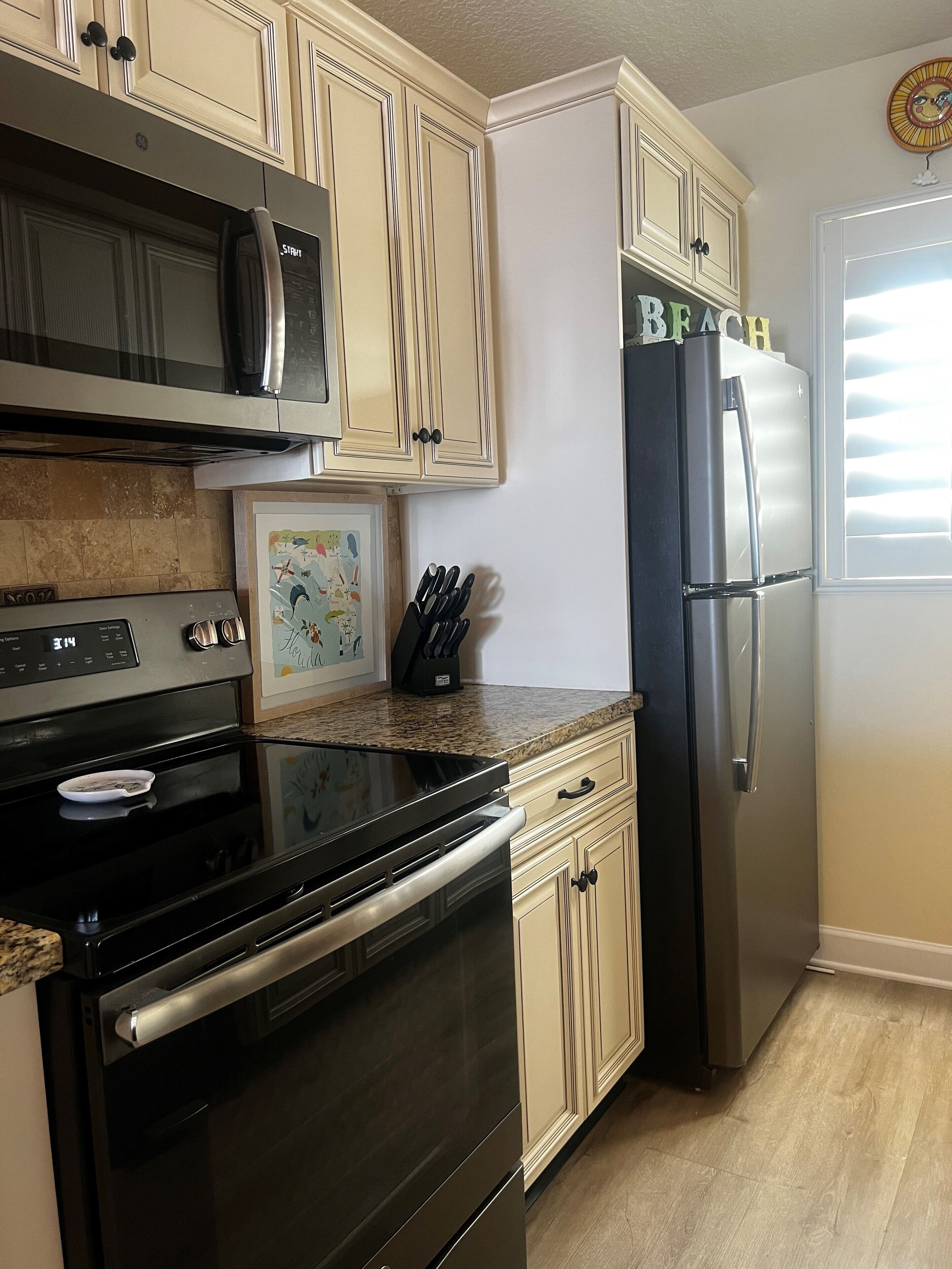 A kitchen with beige cabinetry, a stainless steel refrigerator, a microwave, and an oven.