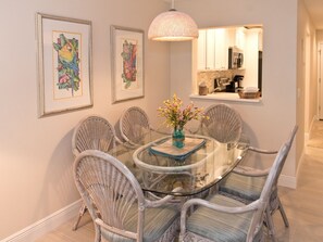 A dining area with a round glass table surrounded by wicker chairs, a vase with flowers, and framed artwork on the wall.