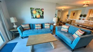 A modern living room with a blue sofa set, a wooden coffee table, and a painting of oranges on the wall. - Don't miss this direct Oceanfront view at the beloved Summerhouse 254 (St. Augustine)