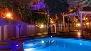 Une piscine dotée d’une terrasse en bois, entourée d’une clôture blanche et de palmiers.