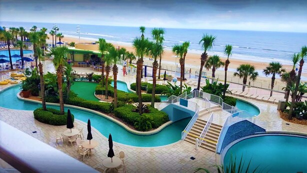 Ein Poolbereich eines Resorts mit mehreren Schwimmbecken, Palmen und Blick auf den Strand.