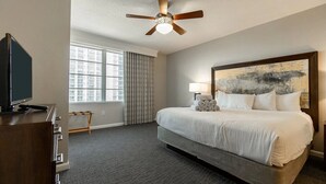 Ein Hotelzimmer mit einem großen Bett, einem Deckenventilator, einem Fernseher, einem Fenster mit Vorhängen und einem Gemälde an der Wand.