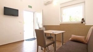 A room with a wooden floor, a sofa, a table, and a TV mounted on the wall.