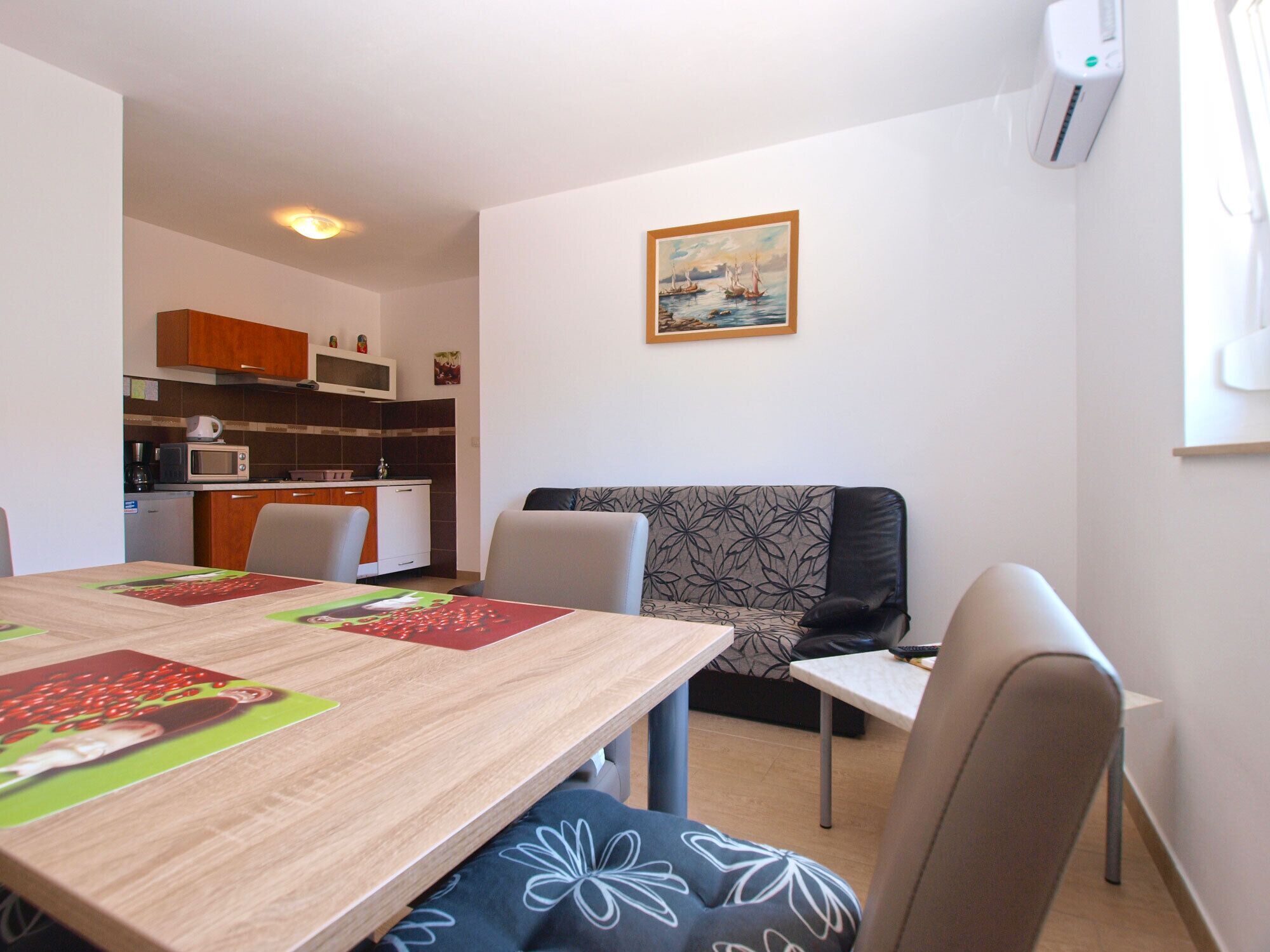 Un espace de vie compact comprenant une table à manger, des chaises, un canapé, un coin cuisine et un tableau accroché au mur.