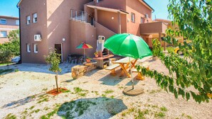 A multi-story building with a patio area featuring outdoor furniture, a grill, and a green umbrella.