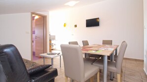 A modern living room with a dining area, a flat-screen TV mounted on the wall, and a door leading to another room.