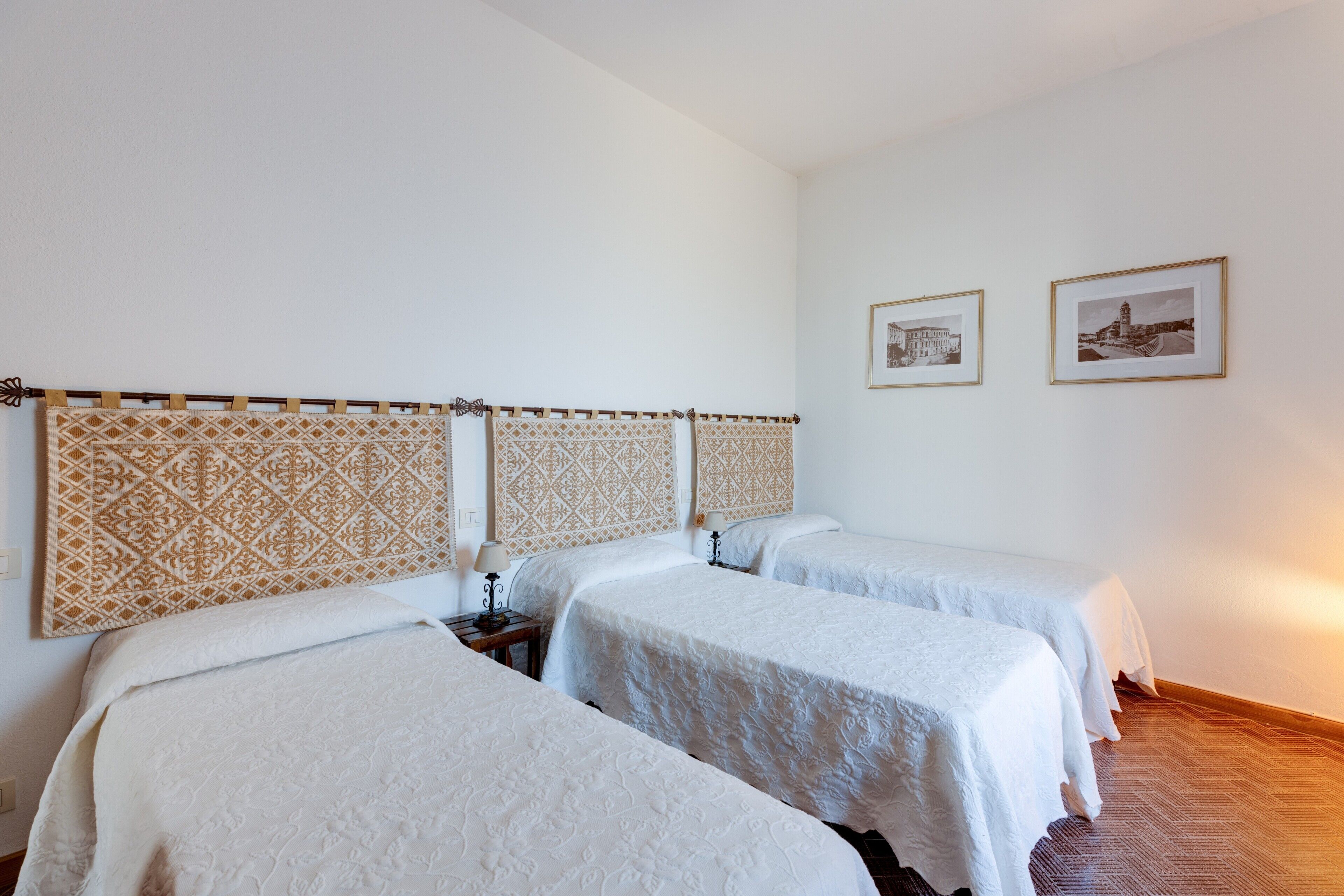 Een hotelkamer met drie bedden, een gestreept hoofdeinde, een nachtkastje en twee ingelijste foto's aan de muur.