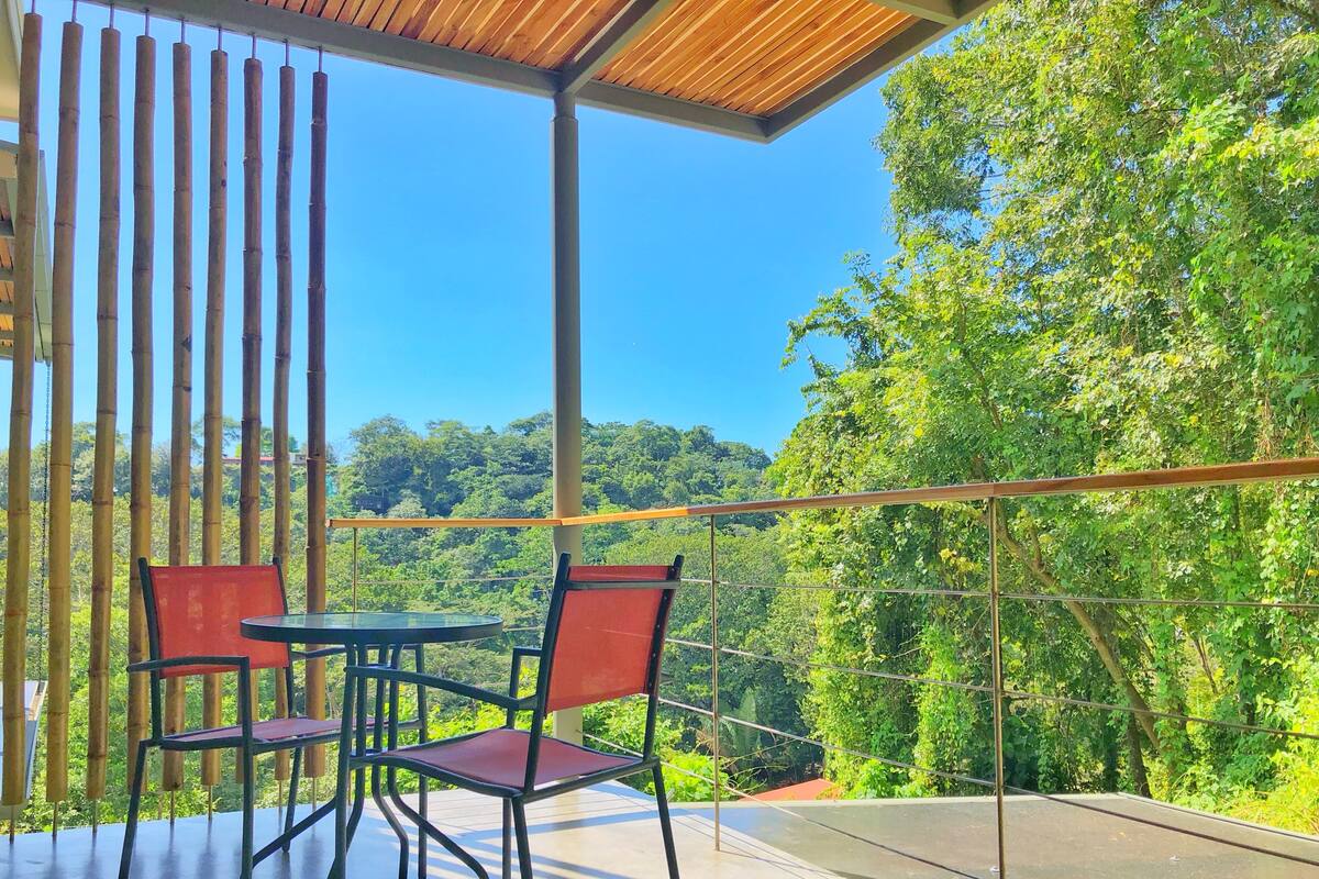 Uma varanda com mesa e cadeiras, com vista para uma floresta verde e exuberante.