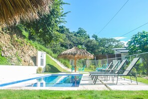 A swimming pool with lounge chairs and a thatched umbrella.