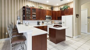 A modern kitchen with wooden cabinets, a central island, a microwave, an oven, and a refrigerator. - Closest to Disney by VillaDirect (Kissimmee)