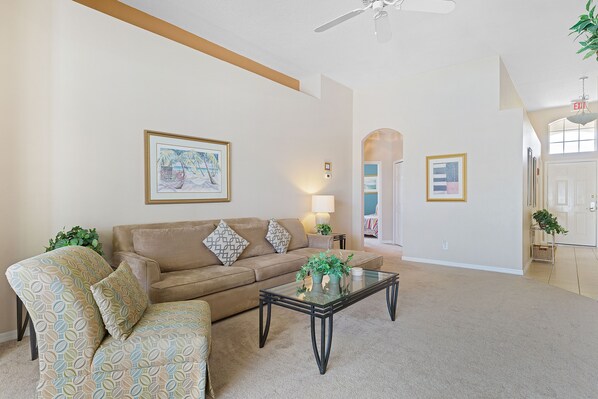 A living room with a beige sofa, a glass coffee table, and a ceiling fan.